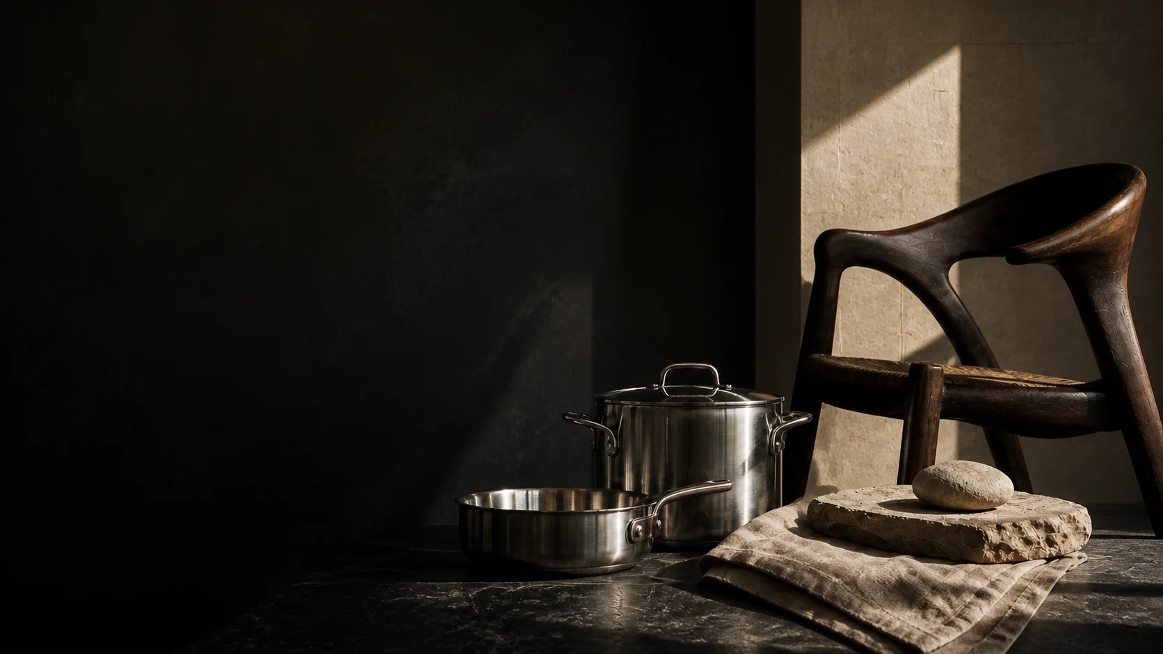 A sculptural chair, cookware, linen and stone in an architectural interior